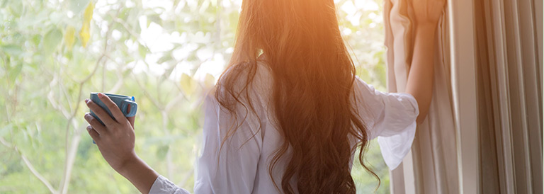 Woman looking outside while holding the curtains.
